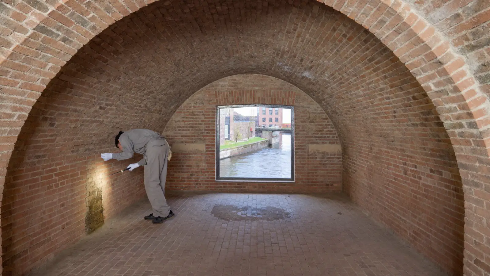 Specialist onderzoekt met een zaklamp een vochtige plek in een gewelfde werfkelder aan de gracht