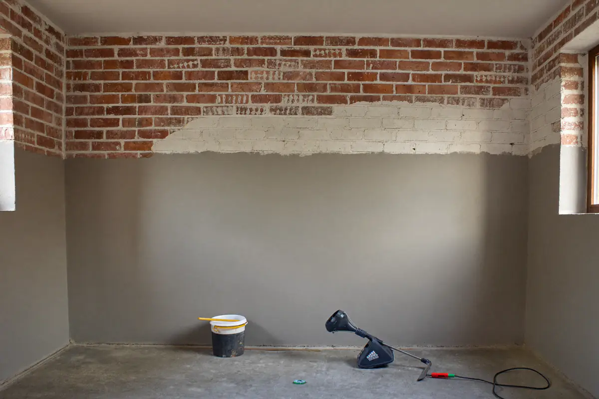 Kelderwand waarvan de onderste helft met grijze afdichtende mortel is bezet en de bovenste helft nog kaal metselwerk is